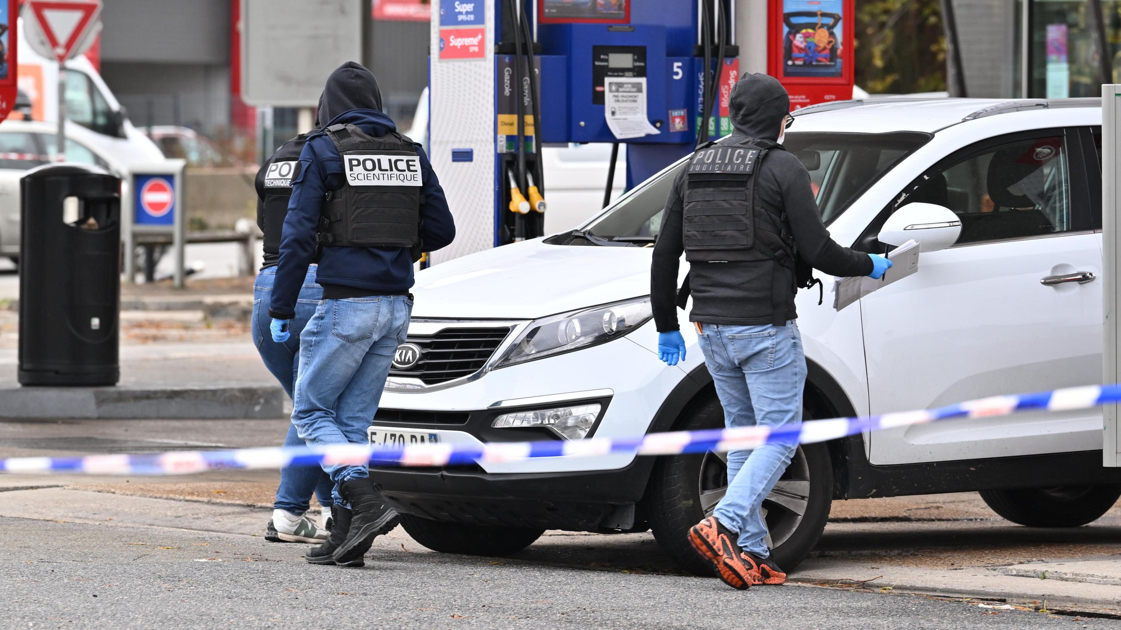 Forensic officers examine evidence at the site of a petrol station where a gunman opened fire from a vehicle