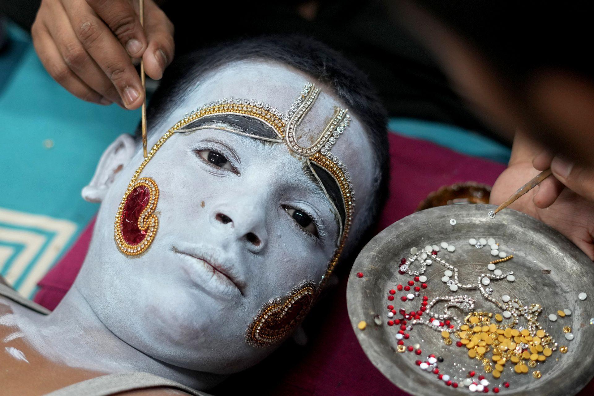 A face‑painted performer in a blue costume with ornate jewellery stands in a crowd in Uttar Pradesh